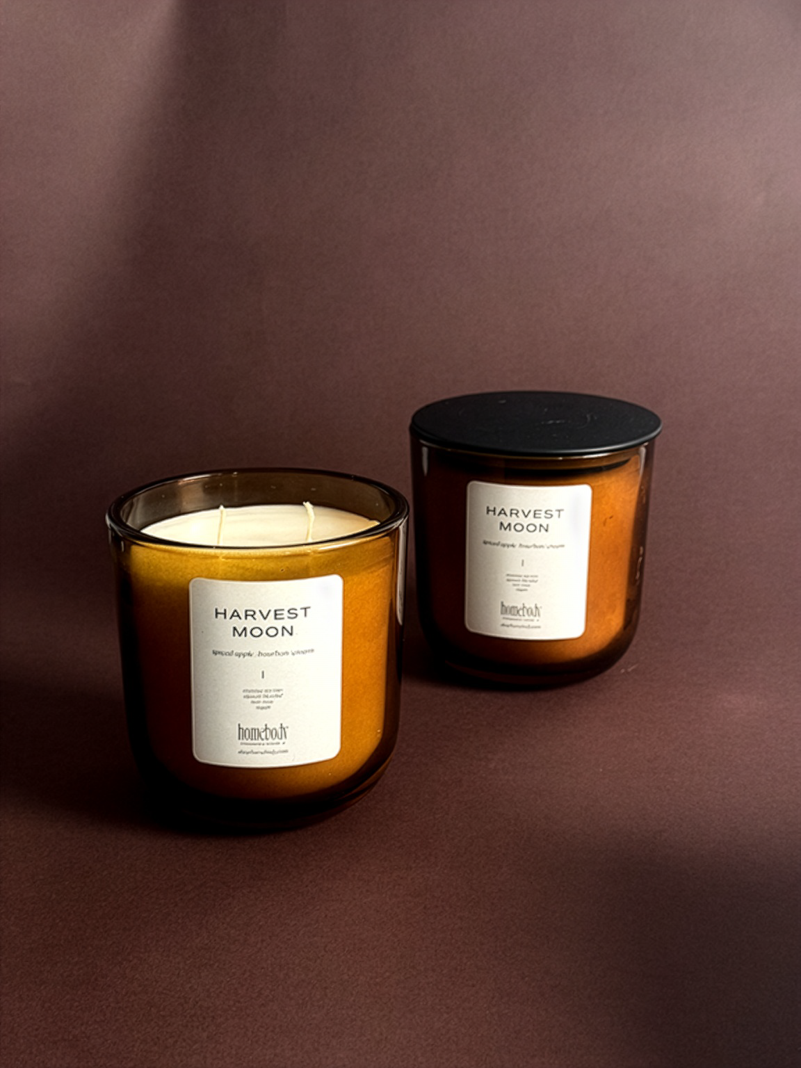 Two 'Harvest Moon' fall-inspired candles on a brown background