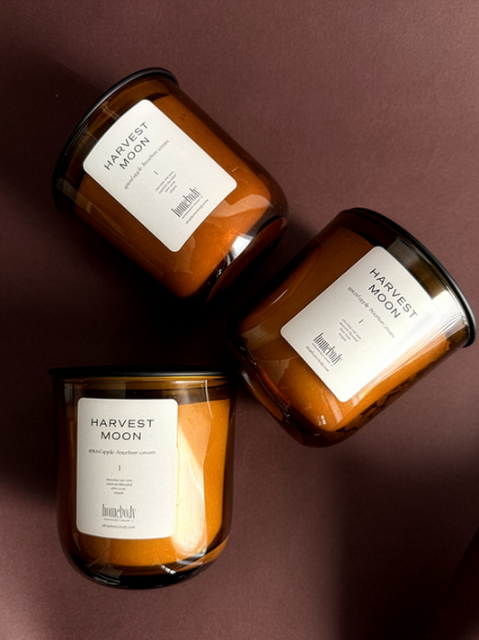 Three 'Harvest Moon' fall-inspired candles on a dark background