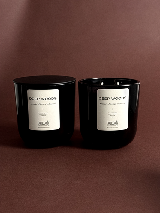 Two black fall candles labeled 'Deep Woods' on a brown background