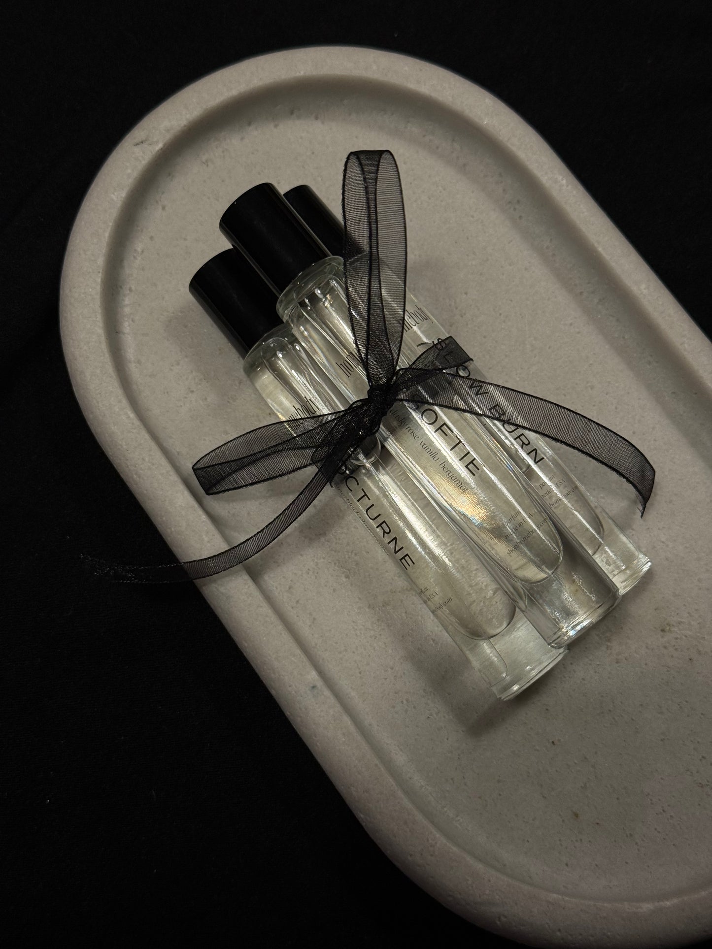 Two small perfume bottles with black ribbons on a gray tray against a black background